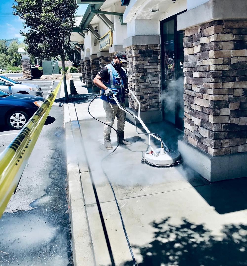 Technician running a surface cleaner along a storefront walkway behind caution tape